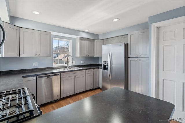 kitchen with wood finished floors, gray cabinets, a sink, appliances with stainless steel finishes, and dark countertops