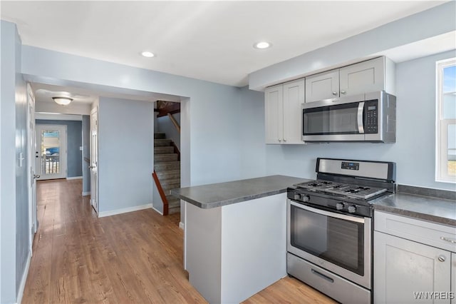 kitchen with dark countertops, light wood-style flooring, appliances with stainless steel finishes, and a peninsula