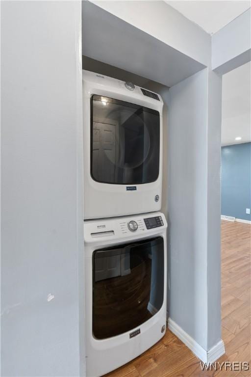 laundry room featuring baseboards, wood finished floors, laundry area, and stacked washer / dryer