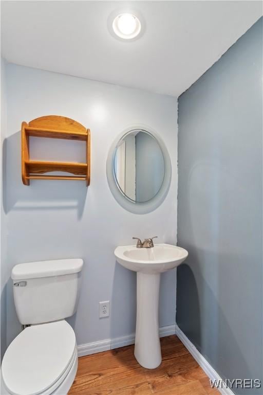 half bath with toilet, wood finished floors, baseboards, and a sink