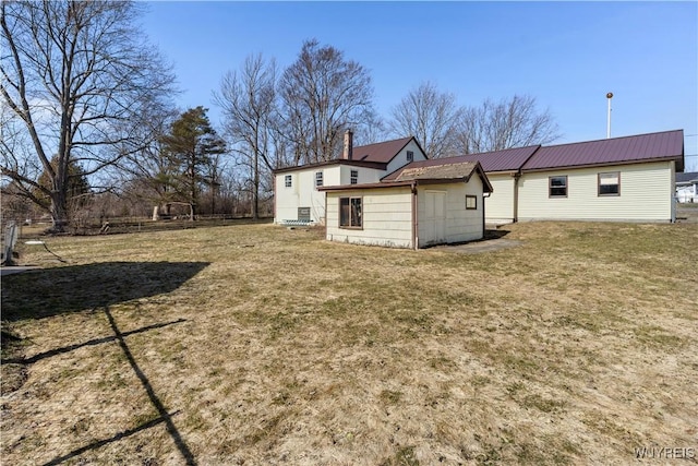 back of house featuring an outbuilding, a lawn, and metal roof