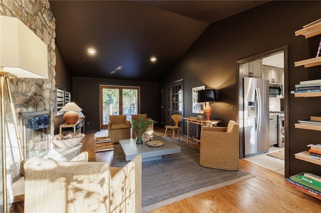 living room featuring lofted ceiling, a stone fireplace, and light wood-style flooring