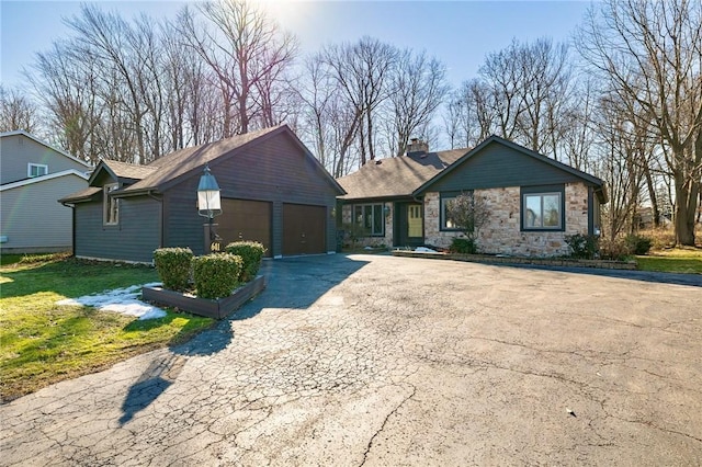 ranch-style house featuring driveway, stone siding, a front yard, an attached garage, and a chimney