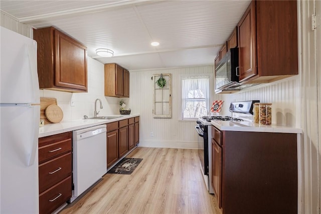 kitchen with baseboards, a sink, black appliances, light countertops, and light wood-type flooring