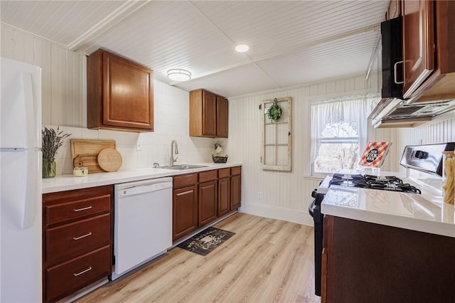 kitchen featuring white appliances, light countertops, light wood finished floors, and a sink