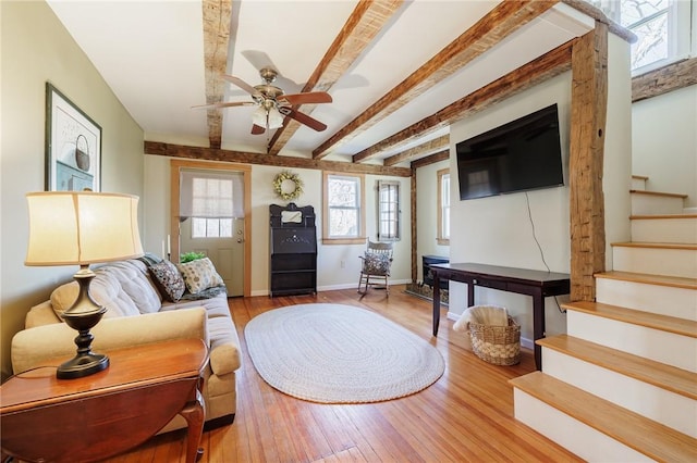 living room with ceiling fan, baseboards, stairway, beamed ceiling, and hardwood / wood-style flooring