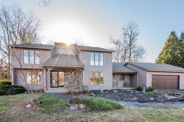 view of front of house with stone siding, an attached garage, and a shingled roof