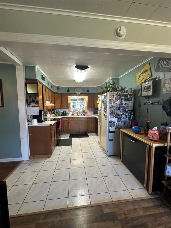 kitchen with brown cabinetry, light countertops, freestanding refrigerator, light tile patterned flooring, and a sink