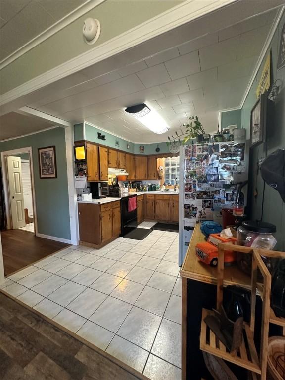 kitchen with black range with electric stovetop, under cabinet range hood, brown cabinetry, light countertops, and light tile patterned floors