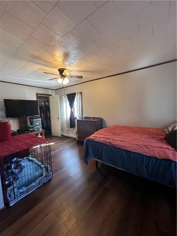 bedroom with a closet, a baseboard heating unit, ceiling fan, and wood finished floors