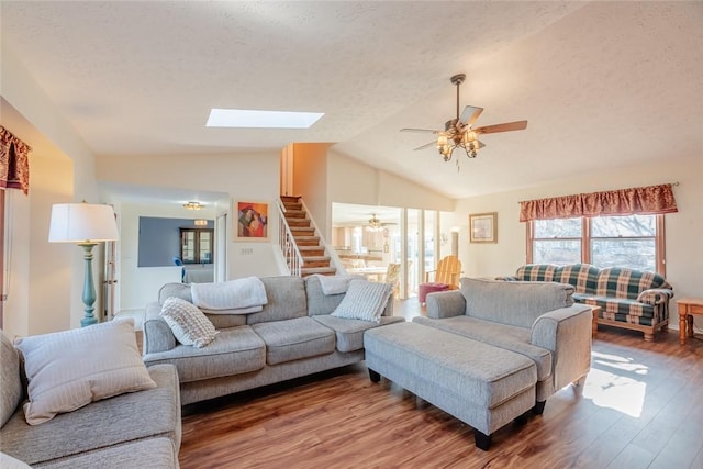 living room featuring lofted ceiling with skylight, a textured ceiling, ceiling fan, and wood finished floors