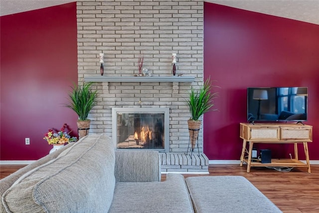 living room with lofted ceiling, a textured ceiling, a brick fireplace, and wood finished floors