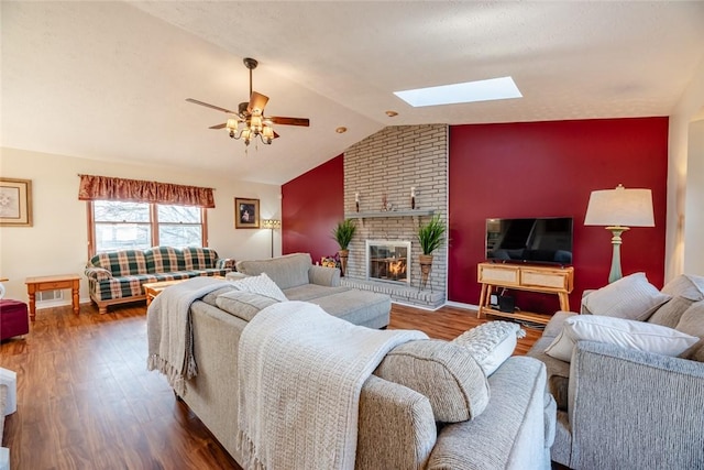 living area with baseboards, ceiling fan, vaulted ceiling with skylight, a fireplace, and wood finished floors