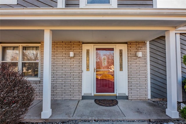 view of exterior entry featuring brick siding and covered porch