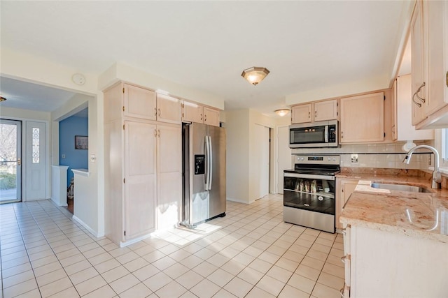 kitchen with a sink, stainless steel appliances, light tile patterned floors, decorative backsplash, and light stone countertops