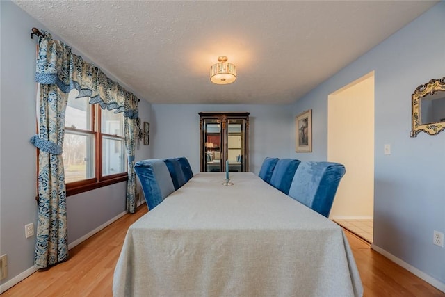 dining space featuring light wood-style flooring, a textured ceiling, and baseboards