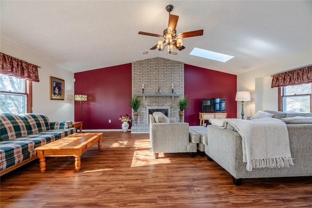 living area featuring a fireplace, lofted ceiling with skylight, wood finished floors, and a ceiling fan