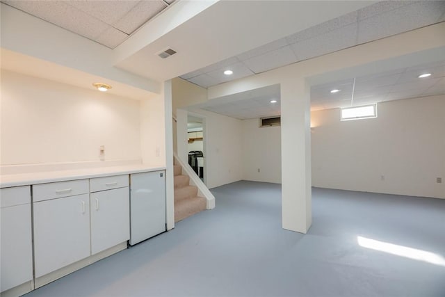 basement with visible vents, a drop ceiling, fridge, recessed lighting, and stairs