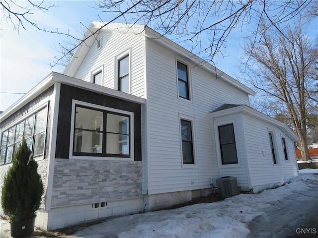 view of snowy exterior featuring central AC unit, stone siding, and crawl space