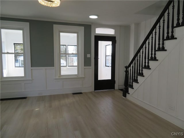 entrance foyer with stairway, visible vents, wood finished floors, and a decorative wall