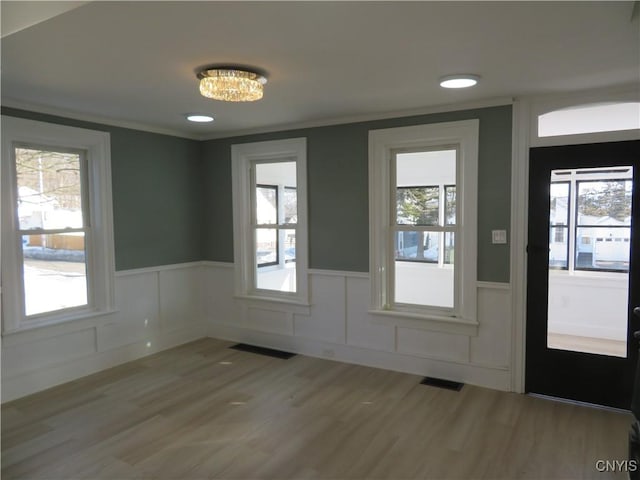 foyer with visible vents, light wood-style floors, a wainscoted wall, and ornamental molding