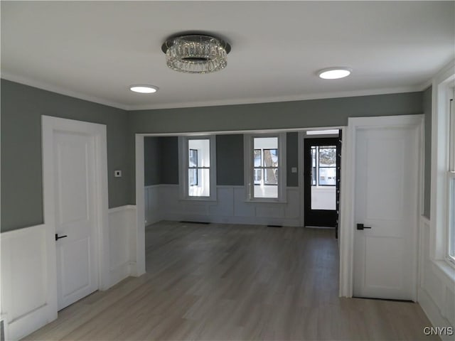 corridor with a wainscoted wall, crown molding, a healthy amount of sunlight, and light wood-type flooring