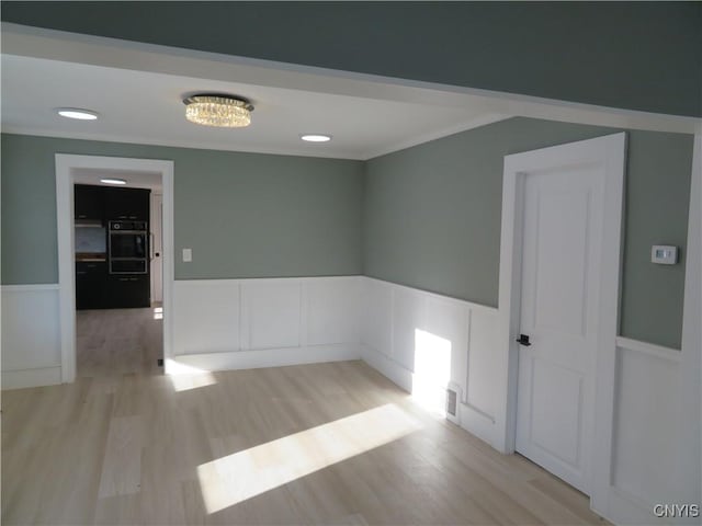 spare room featuring crown molding, light wood-style flooring, and a wainscoted wall