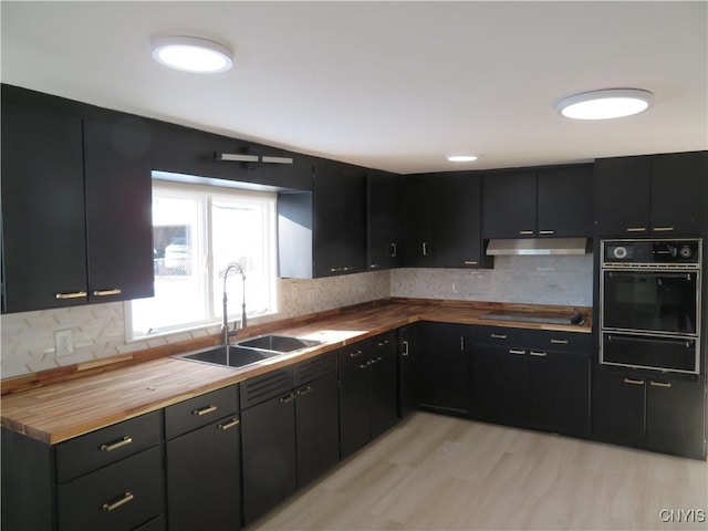 kitchen featuring black appliances, a sink, wood counters, under cabinet range hood, and dark cabinetry