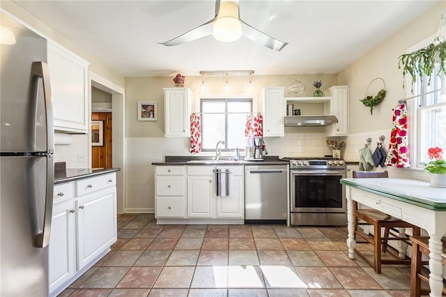 kitchen with a sink, under cabinet range hood, dark countertops, stainless steel appliances, and white cabinets