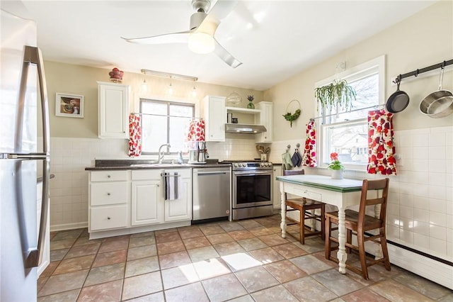 kitchen featuring under cabinet range hood, appliances with stainless steel finishes, white cabinets, tile walls, and a sink