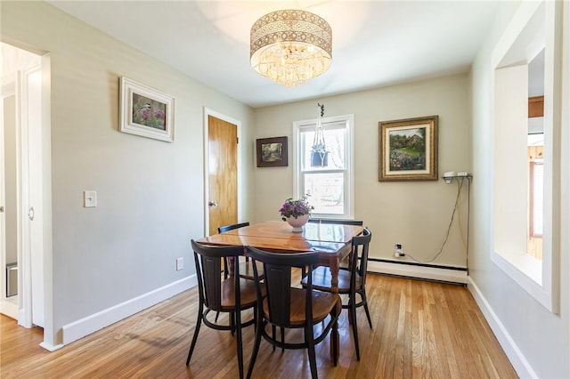 dining space with a baseboard heating unit, light wood-style floors, and baseboards