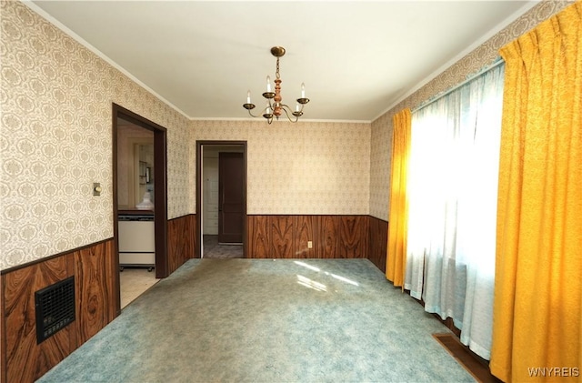 carpeted spare room featuring visible vents, a notable chandelier, wallpapered walls, crown molding, and wainscoting