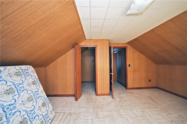 unfurnished bedroom featuring wooden walls, baseboards, and vaulted ceiling