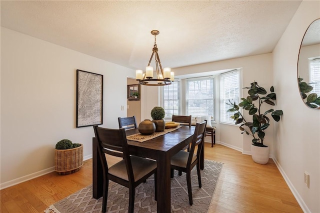 dining space with a notable chandelier, light wood-style flooring, a textured ceiling, and baseboards