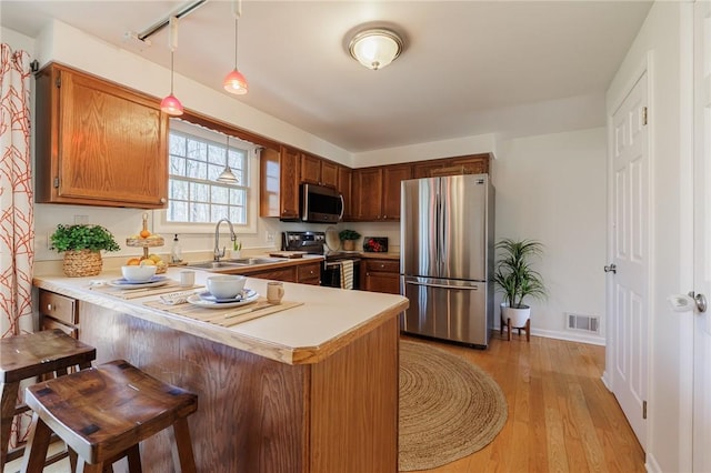 kitchen with visible vents, a sink, light wood-style floors, appliances with stainless steel finishes, and a peninsula