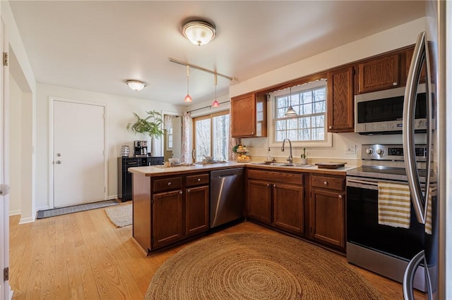 kitchen with a peninsula, light wood-style flooring, a sink, stainless steel appliances, and light countertops