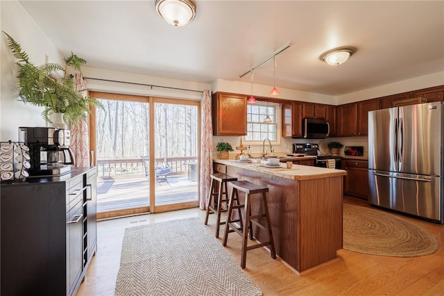 kitchen featuring light wood finished floors, a kitchen breakfast bar, appliances with stainless steel finishes, and a peninsula