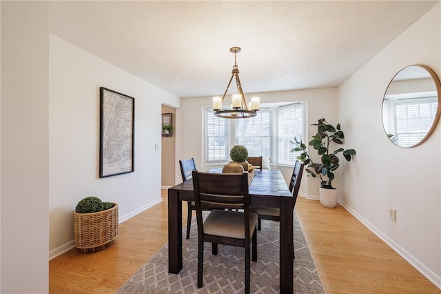 dining area with light wood-type flooring, baseboards, and a notable chandelier