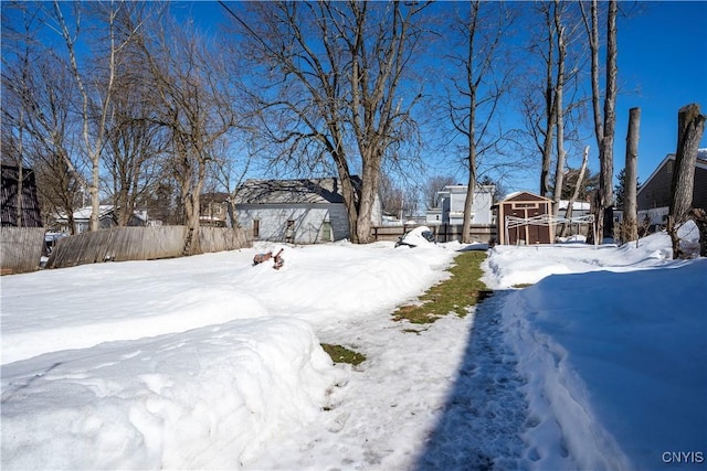 yard covered in snow with a storage shed, an outdoor structure, and fence