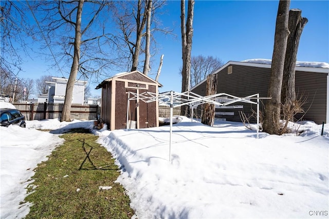 yard layered in snow featuring a storage shed, an outdoor structure, and fence