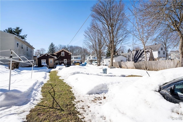 snowy yard featuring a residential view, a garage, and fence