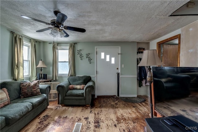 living room featuring a ceiling fan, wood finished floors, visible vents, and a textured ceiling