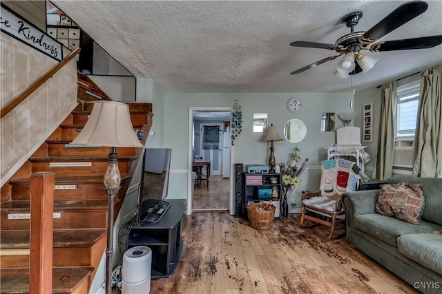 living area with ceiling fan, cooling unit, wood finished floors, and a textured ceiling