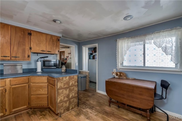 kitchen featuring dark countertops, dark wood-style floors, baseboards, stainless steel microwave, and brown cabinets