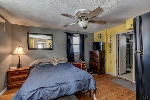 bedroom featuring wood-type flooring, a ceiling fan, baseboards, and freestanding refrigerator