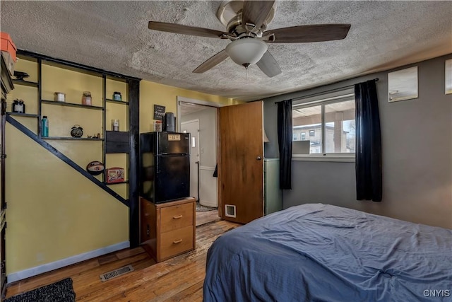 bedroom with visible vents, a textured ceiling, wood finished floors, freestanding refrigerator, and baseboards