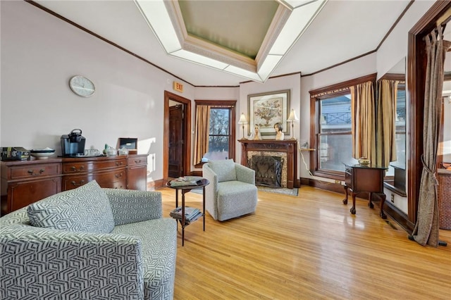 living area featuring light wood-type flooring, a healthy amount of sunlight, a raised ceiling, and crown molding