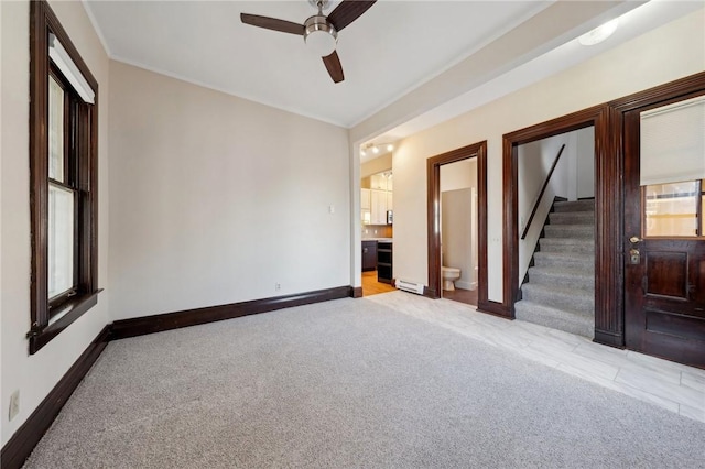 empty room featuring a baseboard heating unit, stairway, light colored carpet, and baseboards