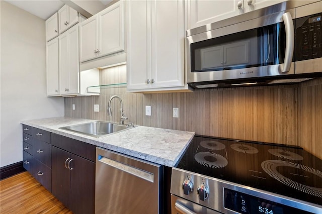 kitchen with a sink, stainless steel appliances, white cabinetry, light wood-type flooring, and backsplash