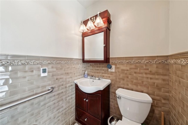 bathroom with a wainscoted wall, toilet, tile walls, and vanity